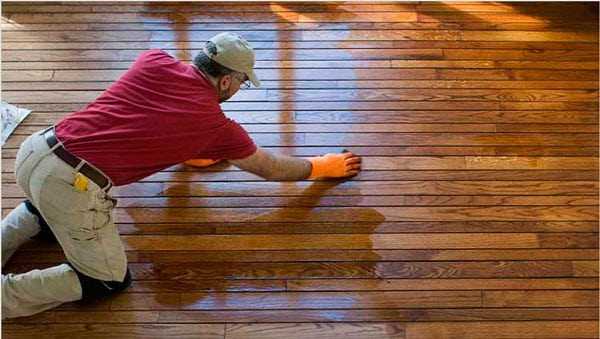 Мужчина натерает пропитывает пол Пропитанный деревянный пол