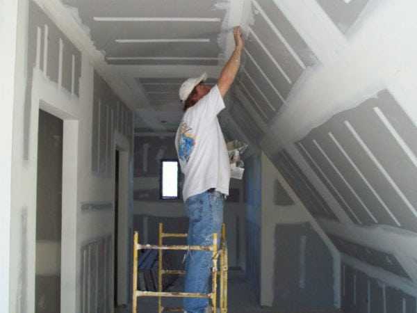 Шпаклевка гипсокартона Мужчина шпаклюет гипсокартон